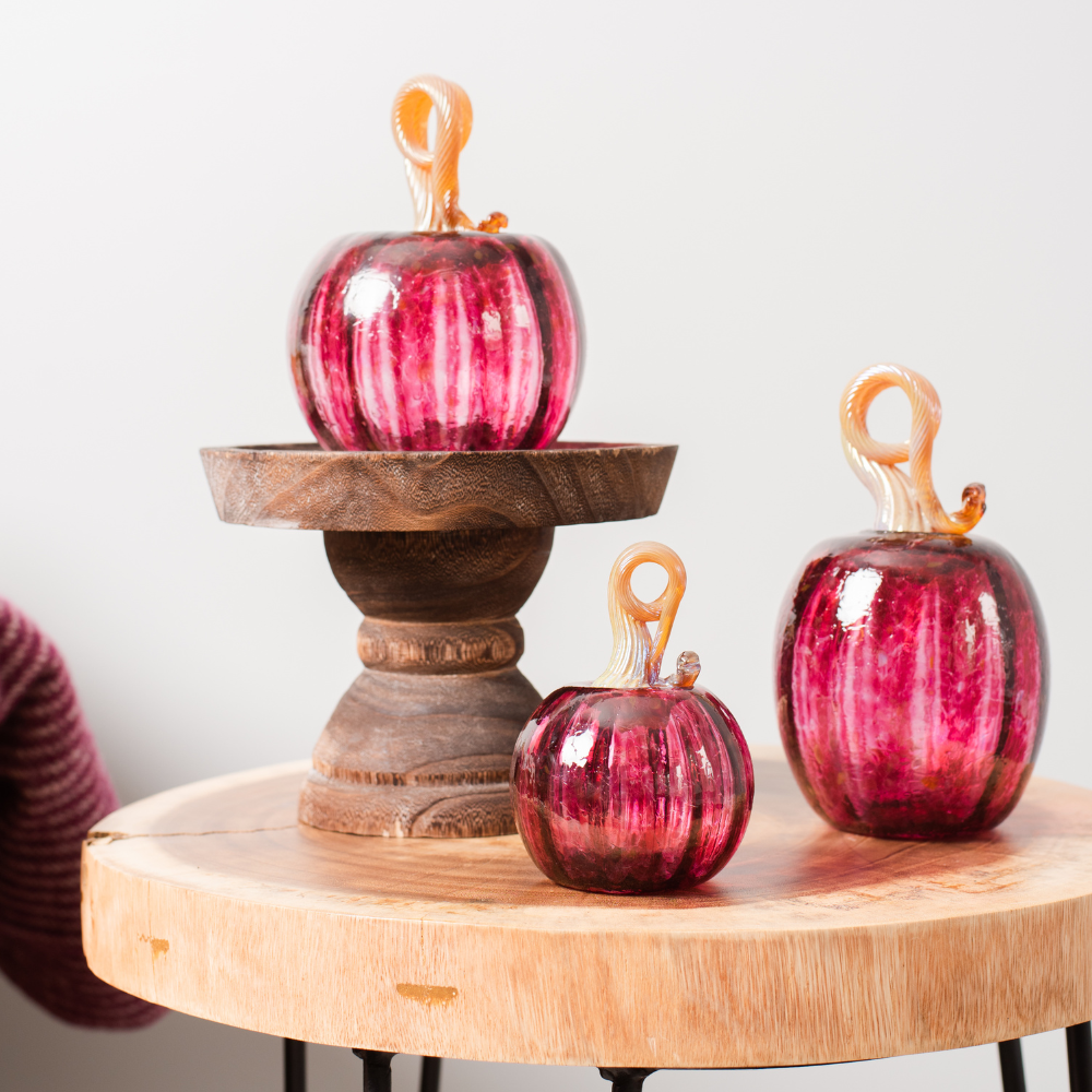 6" Cranberry Round Pumpkin on wood pedestal.  3" Round and Oval Cranberry Pumpkins on a wood table. 