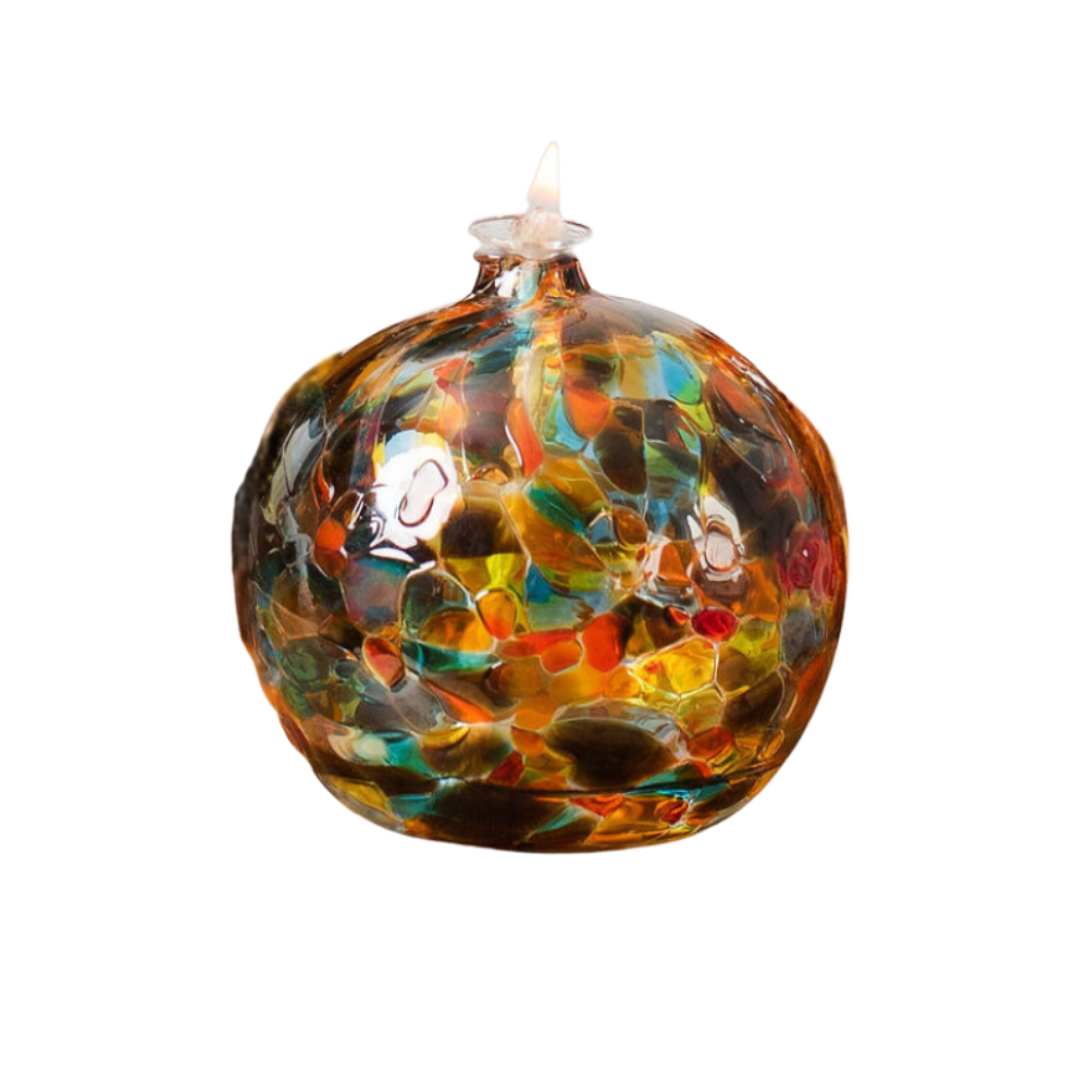 Round glass ball with flat base and wick with brown, blue, red, lime, and orange glass mosaiced around the entire surface on a transparent background.