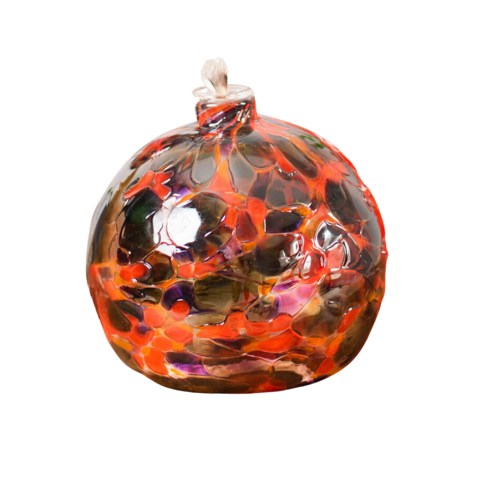 Round glass ball with flat base and wick with purple, orange and grey glass mosaiced around the entire surface on a transparent background.