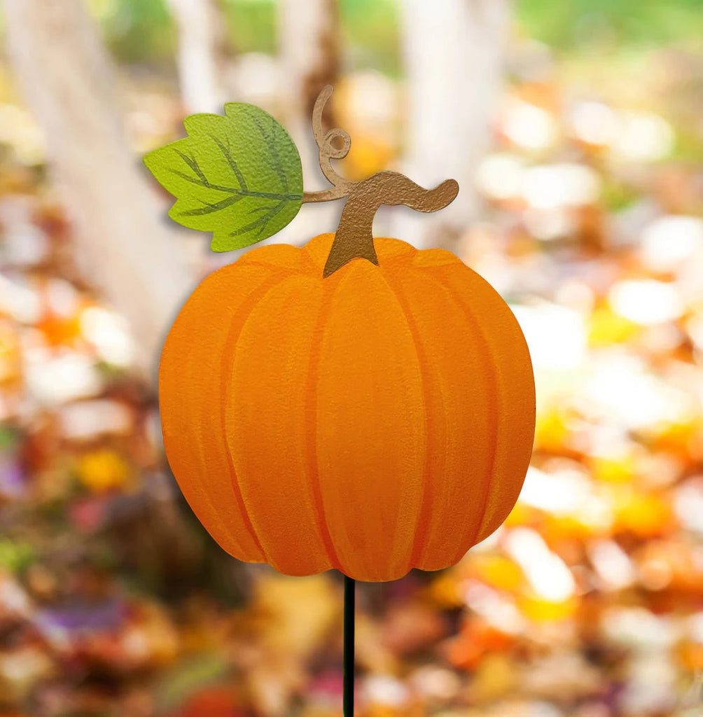 Large pumpkin magnet on a garden stake in front of a fall forest. 