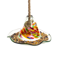What looks like a glass hat with a ripple brim full of birdseed. The cone of has orange, purple, red, green and yellow glass swirled into clear glass. A rope comes out of a hole in the top. 