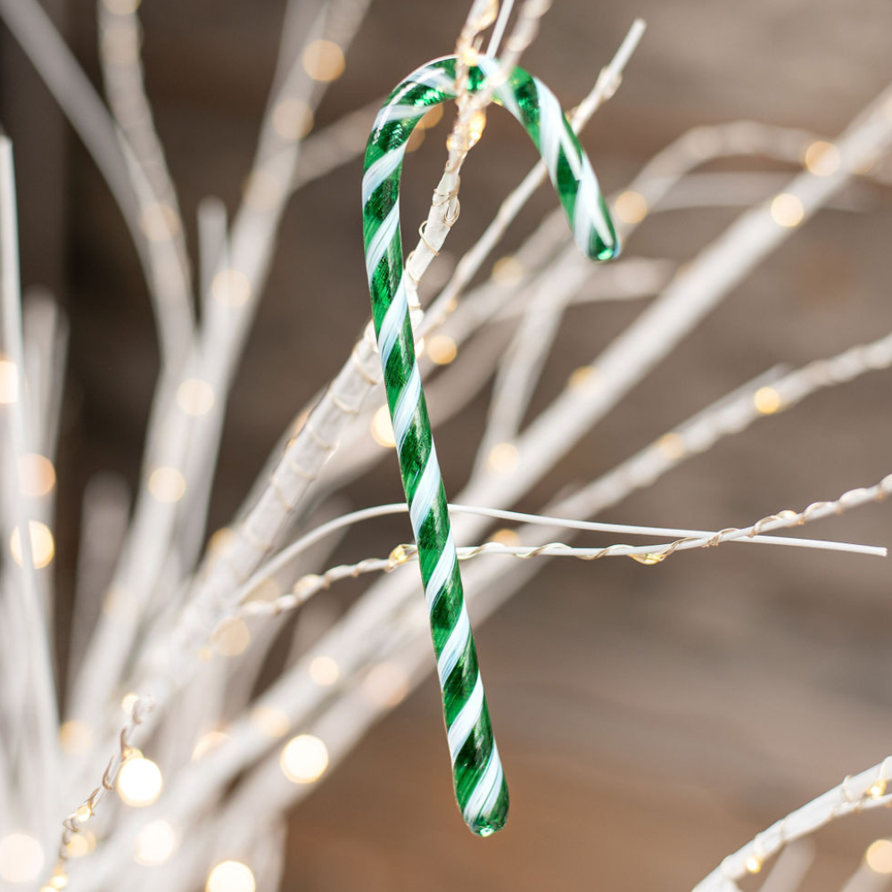 Green and white striped glass Candy Cane on white branches with twinkle lights. 