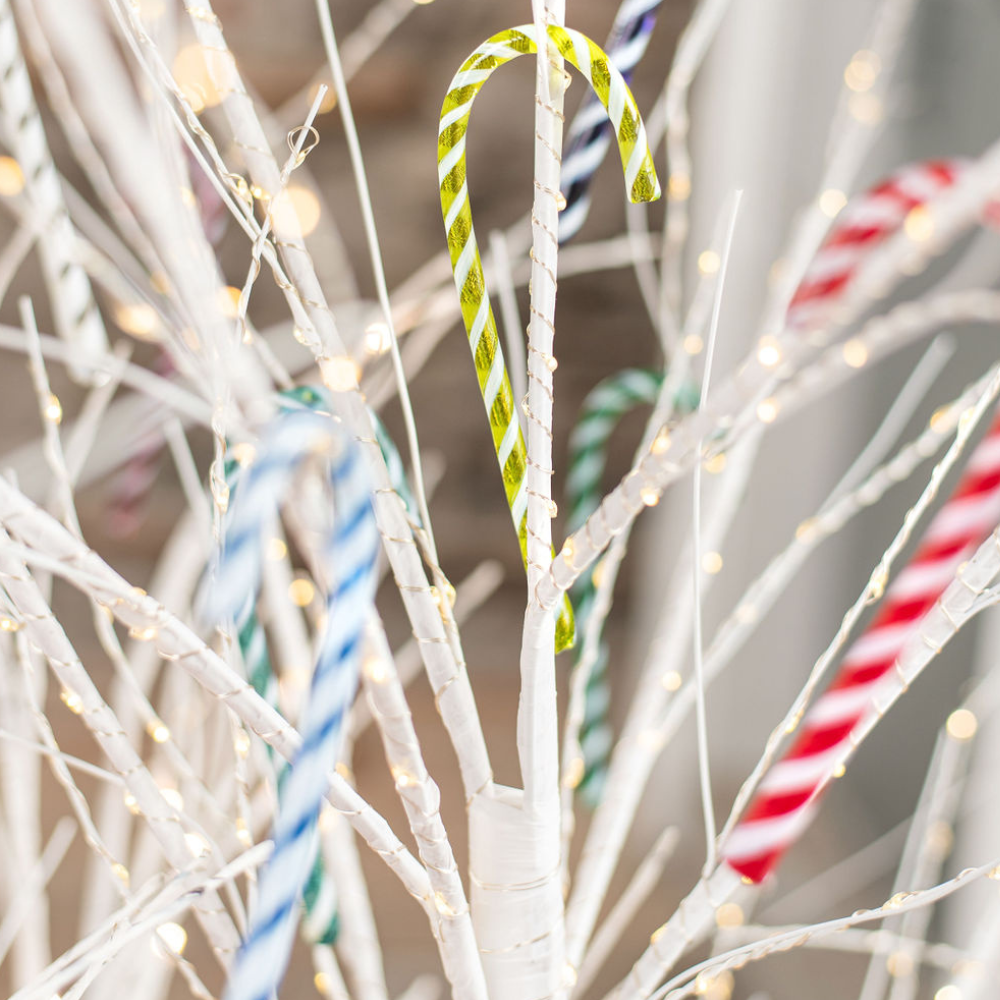 Assorted glass Candy Canes on white branches with twinkle lights.