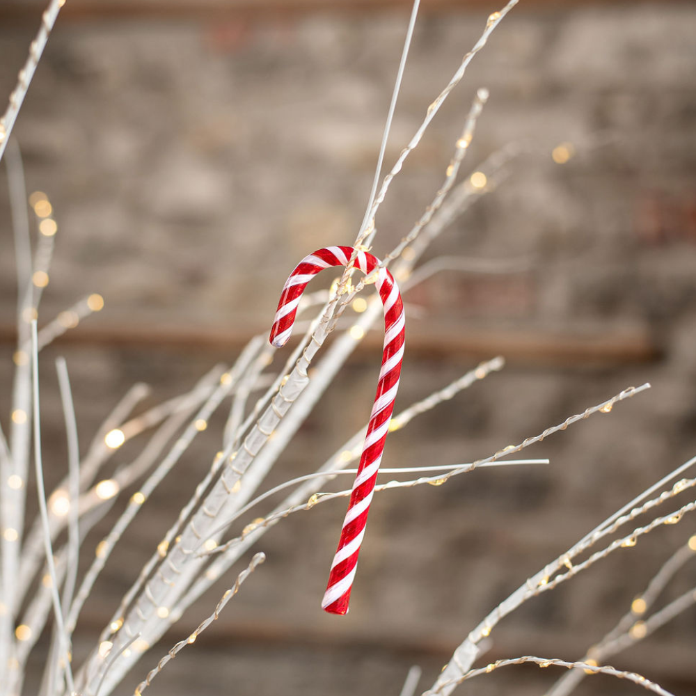 Red and white striped glass Candy Cane on white branches with twinkle lights