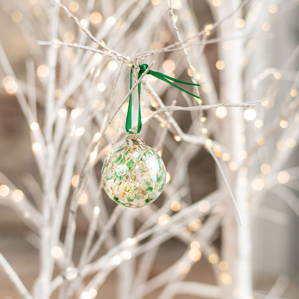 Round glass ball with green, red and opaque white glass mosaiced around the entire surface displayed on a white tree with twinkle lights.