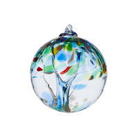 Clear glass orb with lime and blue glass pulled through the middle and blue, green, shimmery gold-copper, red and yellow bits on top on a transparent background.