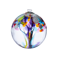 Clear glass orb with purple, orange, yellow and blue glass pulled through the middle and yellow, white, red, purple, pink, orange and blue bits on top on a transparent background.