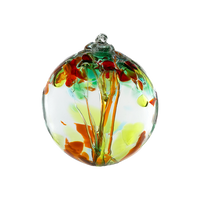 Clear glass orb with pink glass pulled through the middle and yellow, red, orange, tree and gold glitter glass bits on top on a transparent background.