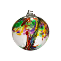 Clear glass orb with red and purple glass pulled through the middle and yellow, red, purple, pink, orange and green glass bits on top on a transparent background.