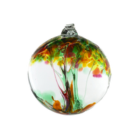 Clear glass orb with green and red glass pulled through the middle and yellow, red, pink, orange, green and brown bits on top on a transparent background.