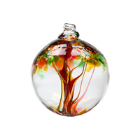 Clear glass orb with orange glass pulled through the middle and yellow, pink, orange, green and amber bits on top on a transparent background.