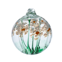 Clear glass orb with a green stem pulled from bottom to top to a canopy of white opaque glass blossoms and orange centres on a transparent background.